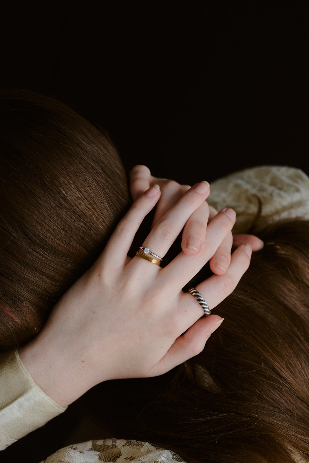 髪に手を添え、ゴールドの結婚指輪にダイヤの指輪とねじりのリングを重ねた手元